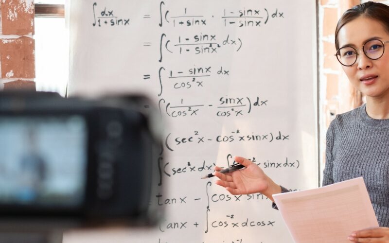 woman recording video of herself teaching at a whiteboard with calculus formulas written on it