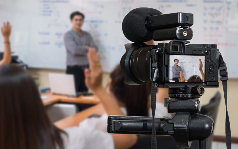 Camera with microphone on tripod recording instructor in classroom for live streaming