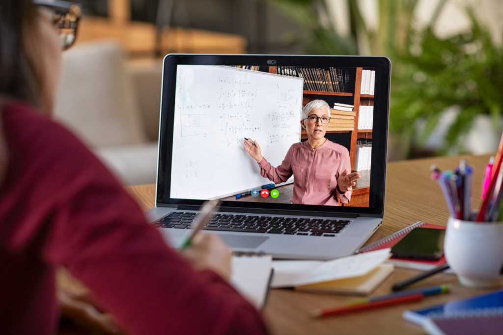 Student watching live classroom lesson where female professor is pointing at content on a whiteboard
