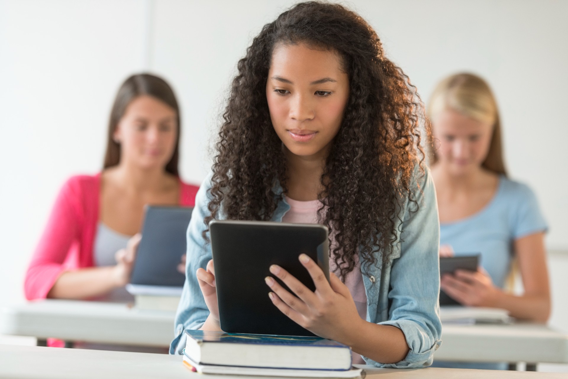 Female students sitting in class with textbooks and notebooks and looking at computer tablets