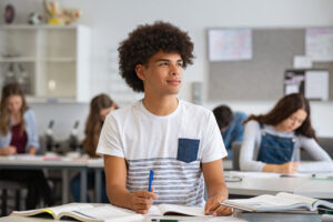 Black male student smiling in class with book open and pen in hand