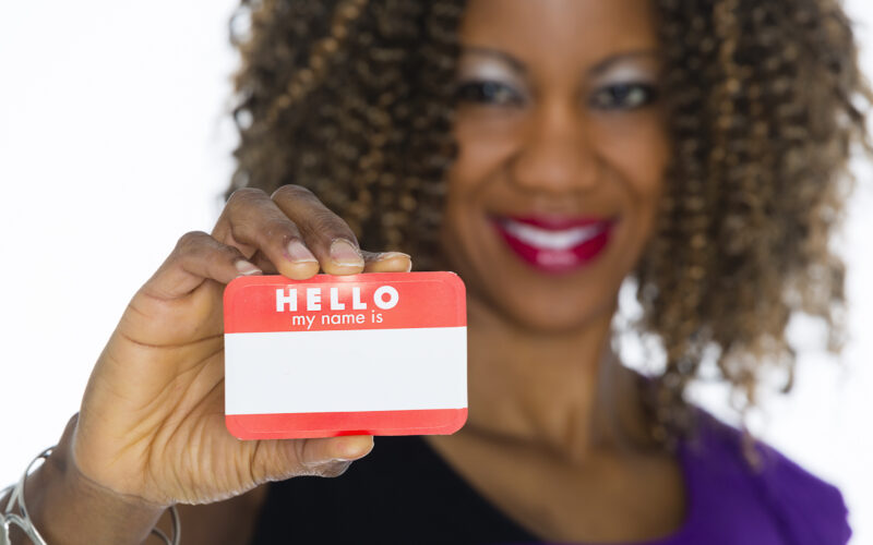 black woman smiling and holding a "Hello my name is" name tag