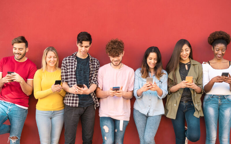 Group of students using smartphones while leaning up against a red wall