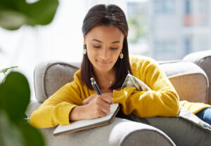 Young woman writing in a journal at home while sitting on couch