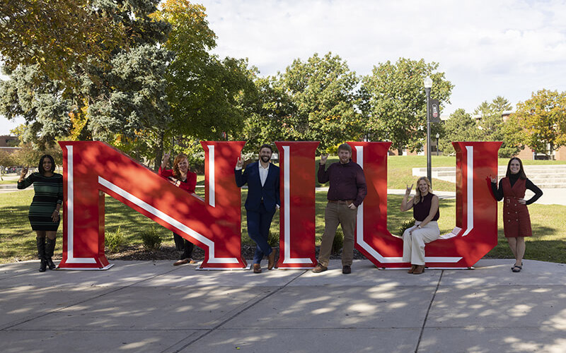 Online Learning staff posing around NIU sign in Martin Luther King, Jr. Commons