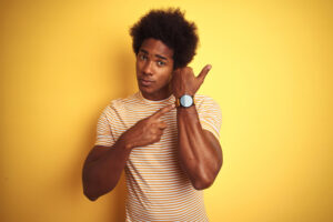 Black young man holding up watch and pointing at it with his finger. 