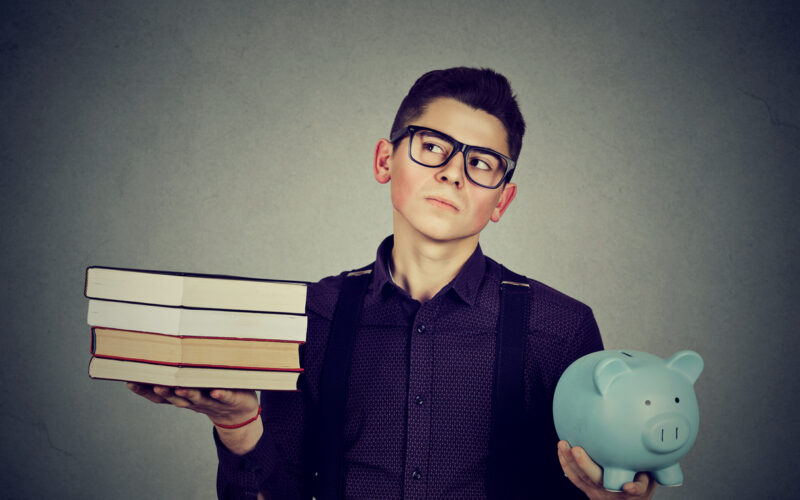 Young man holding a stack pile of books in one hand and a piggy bank in the other hand