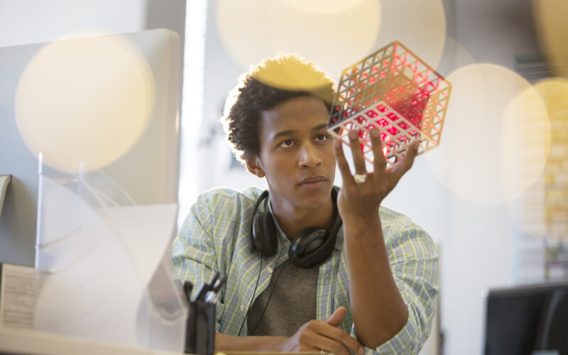Male student examining cube at desk in office