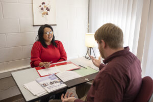 Cynthia Paralejas sitting at desk in QM consultation with man