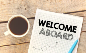 Welcome aboard written on graphing paper on wood table next to a cup of coffee