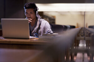 Student wearing headphones working on laptop in library