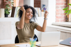 Excited woman raising fists in air and looking at laptop computer