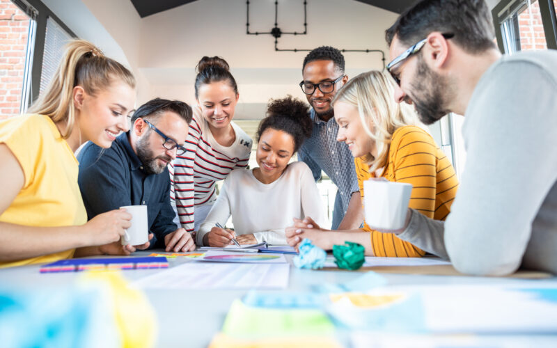 Group of people crowded around a table looking at colorful papers