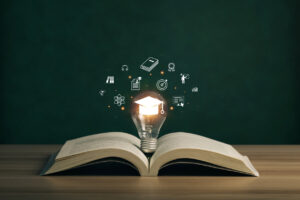 Book open on table with lightbulb lit up with mortarboard cap illuminated inside and icons representing "knowledge" floating around it