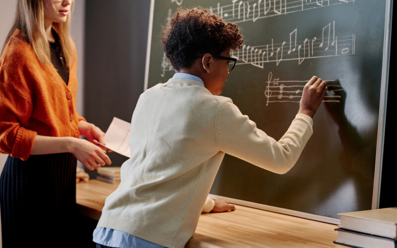Person writing on board in music class with another person watching