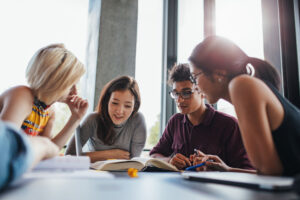 Group of students hovering around a book at a table. 