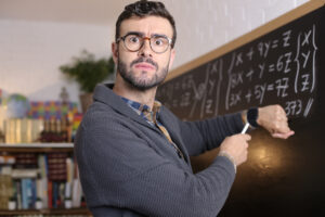 Teacher pointing at wrist watch in classroom.