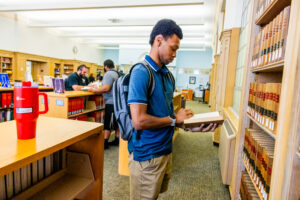 Student reading book in front of book shelves in the Law Library
