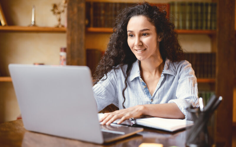 Portrait of woman with dark, curly hair using laptop computer and typing on keyboard