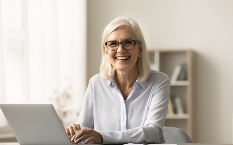 Smiling older female professor typing on laptop