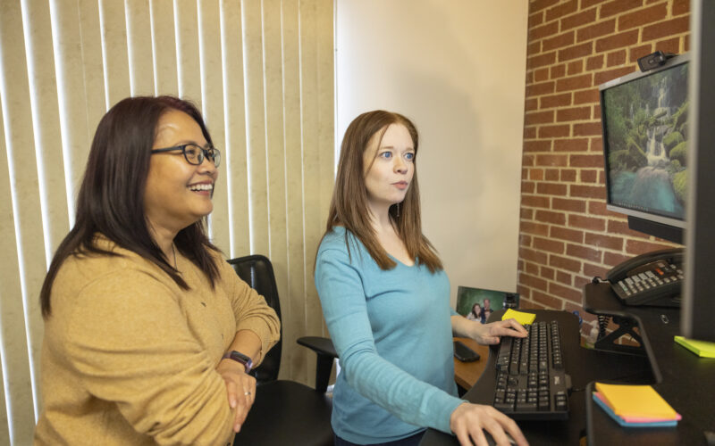 Two women sitting at desk looking at computer monitor