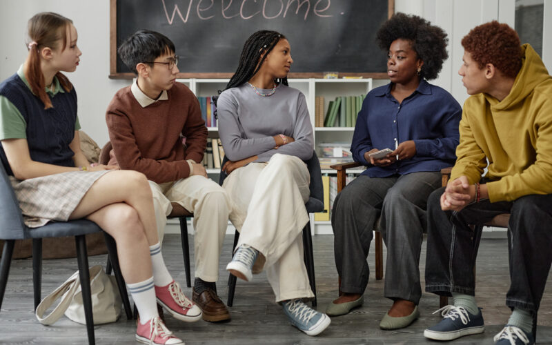 Multiethnic group of people with female professor sitting on chairs in half circle talking