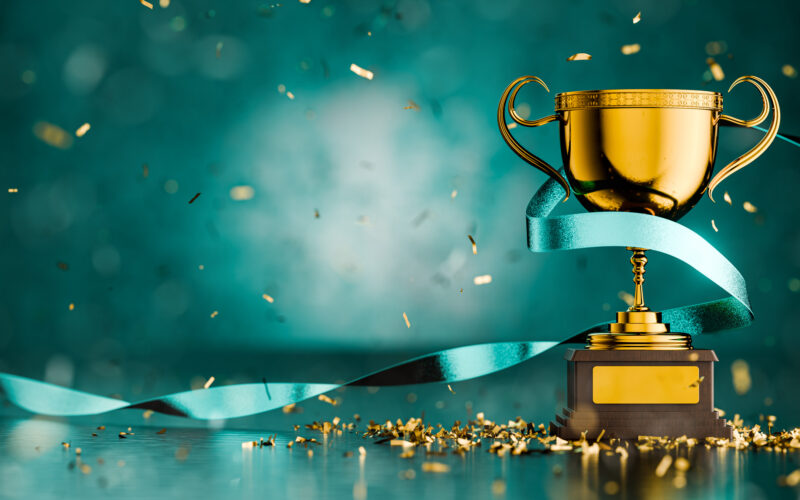 Teal background with award trophy wrapped with a ribbon and gold confetti falling down around it.