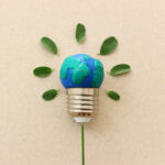 Light bulb with a globe-shaped top representing Earth, surrounded by small leaves arranged like rays, symbolizing environmental sustainability and green energy.