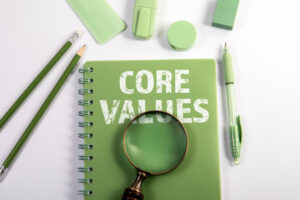 Core Values Text on Green Notebook with Magnifying Glass and Office Supplies on White Background.