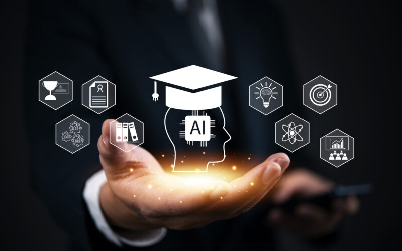 Outstretched hand holds a glowing hologram of a human head with an “AI” chip and graduation cap, surrounded by icons for learning, innovation, analytics, and achievement against a dark background.