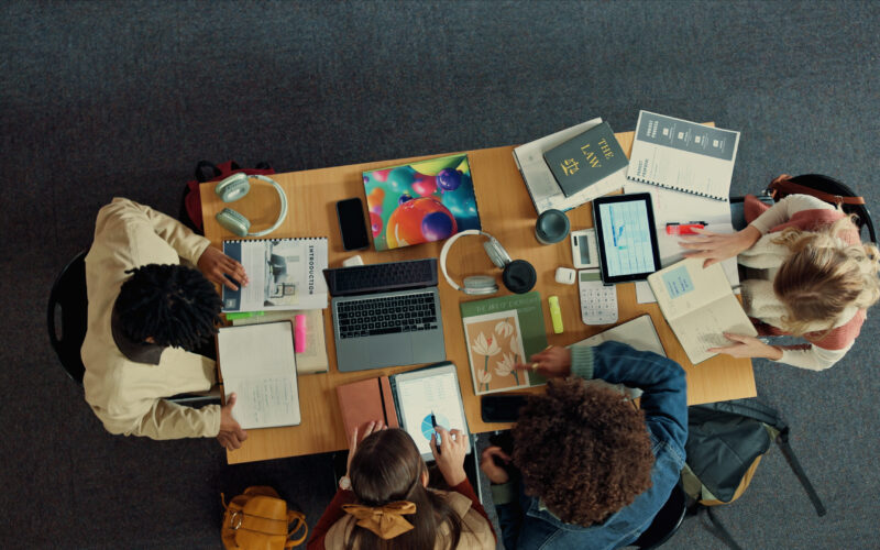 Students sit at a table with different projects spread out among them.
