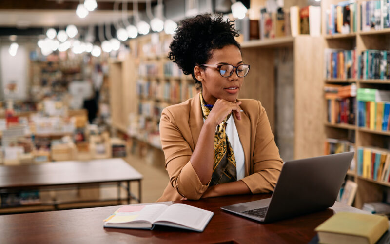 African American female professor using laptop while doing a research at university library.